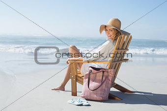 Smiling blonde sitting on wooden deck chair by the sea