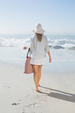 Blonde woman in sunhat carrying beach bag looking out to sea