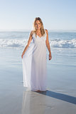 Pretty blonde smiling at camera at the beach in white sundress