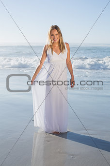 Pretty blonde smiling at camera at the beach in white sundress