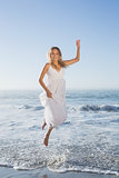 Pretty blonde jumping at the beach in white sundress