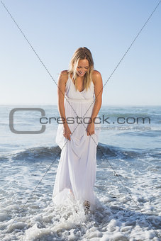 Pretty blonde standing in the sea at the beach in white sundress