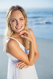 Pretty blonde standing at the beach in white sundress smiling at camera