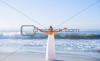 Blonde standing at the beach in white sundress with arms out