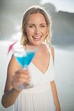Smiling blonde standing at the beach in white sundress with blue cocktail