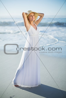 Smiling blonde standing at the beach in white sundress and sunhat