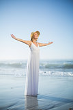 Smiling blonde standing on the beach in white sundress and sunhat