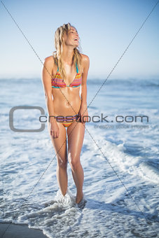 Smiling blonde standing on the beach in bikini