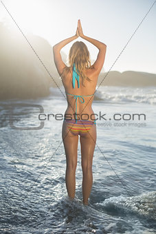 Happy blonde standing on the beach in bikini in tree pose