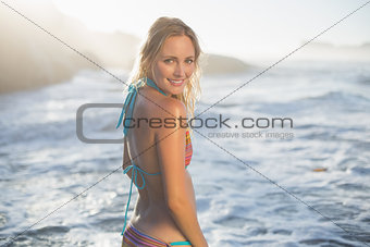 Happy blonde standing on the beach in bikini smiling at camera