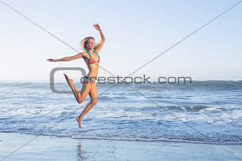 Happy blonde leaping on the beach in bikini