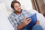 Handsome man lying on couch listening to music on tablet pc