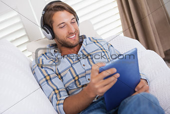Handsome man lying on couch listening to music on tablet pc