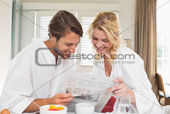 Cute couple in bathrobes having breakfast together reading the newspaper
