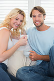 Smiling casual couple sitting on couch having coffee