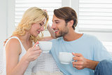 Smiling casual couple sitting on couch having coffee