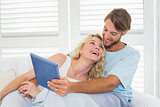 Smiling casual couple sitting on couch under blanket using tablet pc