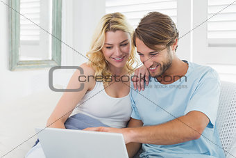 Cute casual couple sitting on couch using laptop