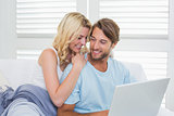 Happy casual couple sitting on couch using laptop
