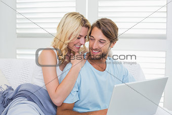 Happy casual couple sitting on couch using laptop