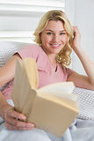 Happy blonde relaxing on the couch with book