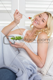 Happy blonde relaxing on the couch eating a salad