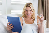 Happy blonde relaxing on the couch with glass of white wine and tablet pc