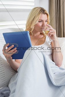 Happy blonde relaxing on the couch with glass of white wine and tablet pc