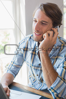Smiling casual man using laptop and talking on smartphone