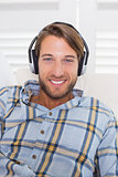 Casual smiling man lying on couch listening to music