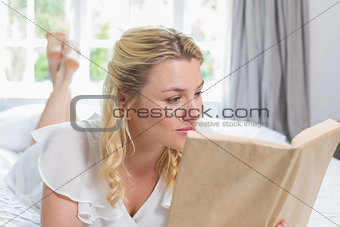 Pretty blonde lying on bed reading a book