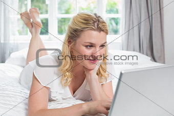 Pretty blonde lying on bed using laptop