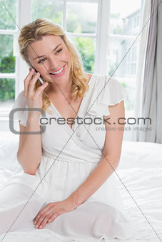 Pretty blonde sitting on bed on the phone