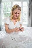 Pretty blonde sitting on bed sending a text message