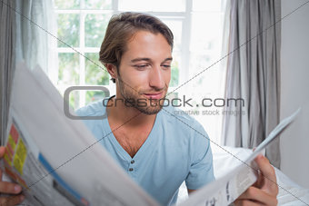 Handsome man sitting on bed reading the newspaper