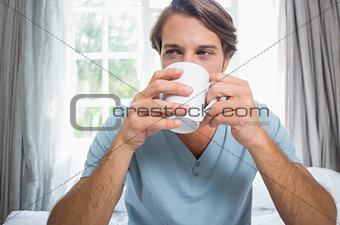 Handsome man sitting on bed drinking coffee