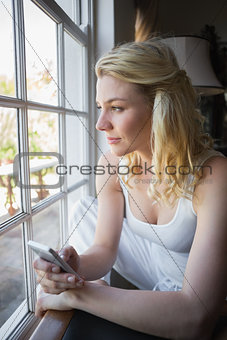 Pretty blonde sitting by the window sending a text