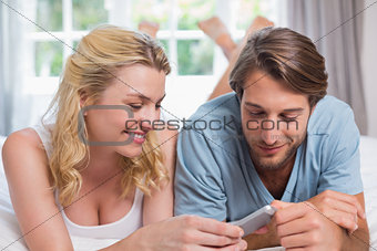Cute couple relaxing on bed looking at smartphone together