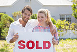 Cute couple standing together in their garden holding sold sign