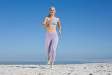 Sporty blonde on the beach jogging towards camera