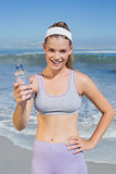 Sporty smiling blonde showing water bottle on the beach
