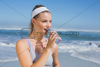 Sporty smiling blonde drinking water on the beach