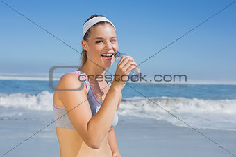 Sporty happy blonde drinking water on the beach