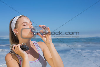 Sporty blonde standing on the beach with bottle and skipping rope