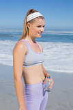 Sporty happy blonde standing on the beach with bottle