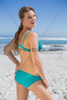 Fit woman in bikini standing on the beach smiling at camera