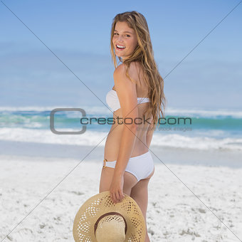 Beautiful happy blonde on the beach in white bikini holding sunhat