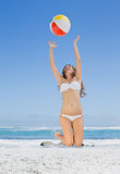 Fit blonde in white bikini throwing beach ball