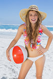 Fit smiling blonde in white bikini and straw hat holding beach ball