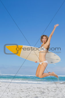 Smiling surfer girl holding her surfboard and jumping on the beach